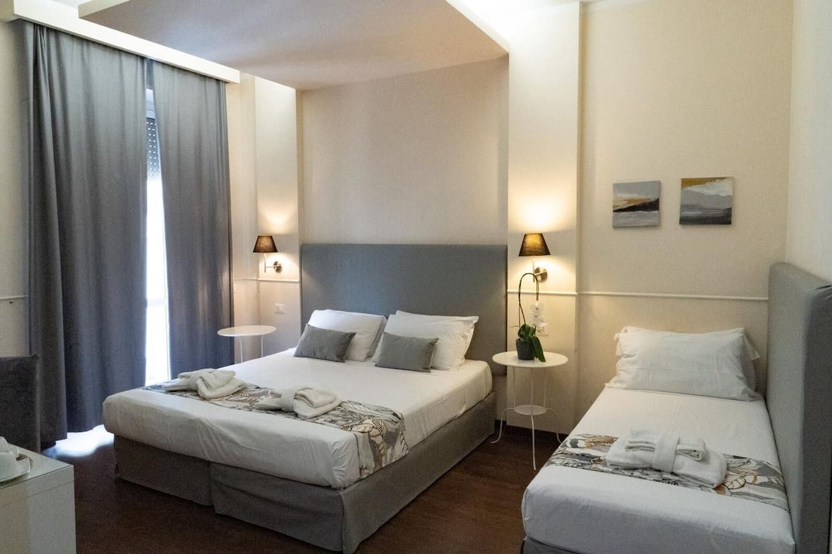 A hotel room with a large bed, two bedside tables, a small table with a plant, and two wall-mounted lamps.