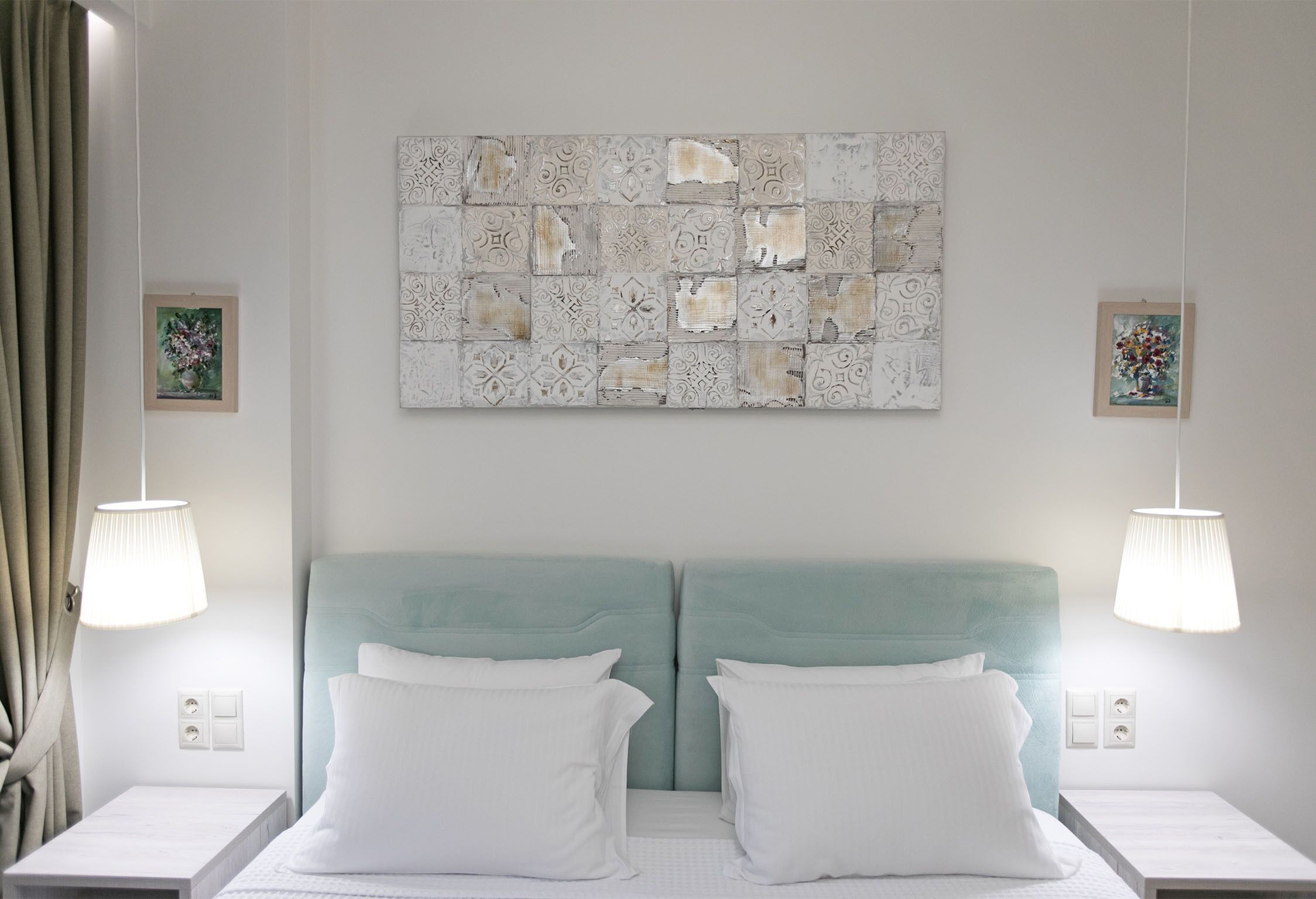 Une chambre d’hôtel avec une grande œuvre d’art décorative accrochée au mur, au-dessus d’un lit double recouvert de linge de lit blanc. Deux lampes de chevet sont placées de part et d’autre du lit.