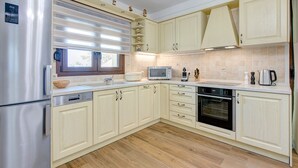 A modern kitchen with light-colored cabinets, stainless steel appliances, a microwave, oven, and a window with blinds.