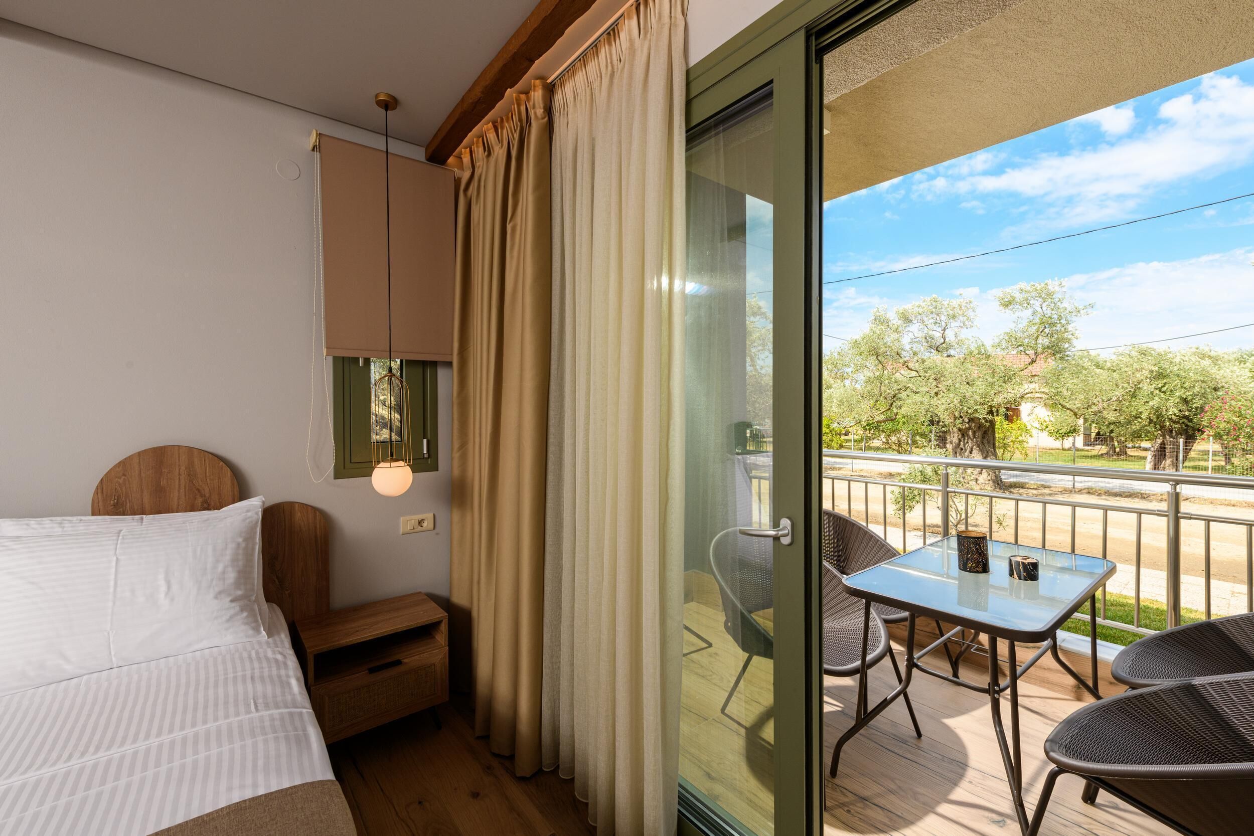 Ein Hotelzimmer mit Bett, kleinem Tisch mit Stühlen, Balkon mit Blick auf Bäume und einer Schiebetür.