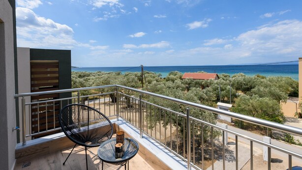 A balcony with a table and chairs, overlooking a coastal landscape with trees and a distant view of the sea. - The Olive Land (Thasos)