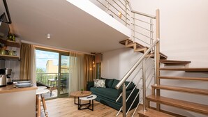 A modern living room with a green sofa, wooden flooring, a small round table, and a staircase with metal railings. - The Olive Land (Thasos)