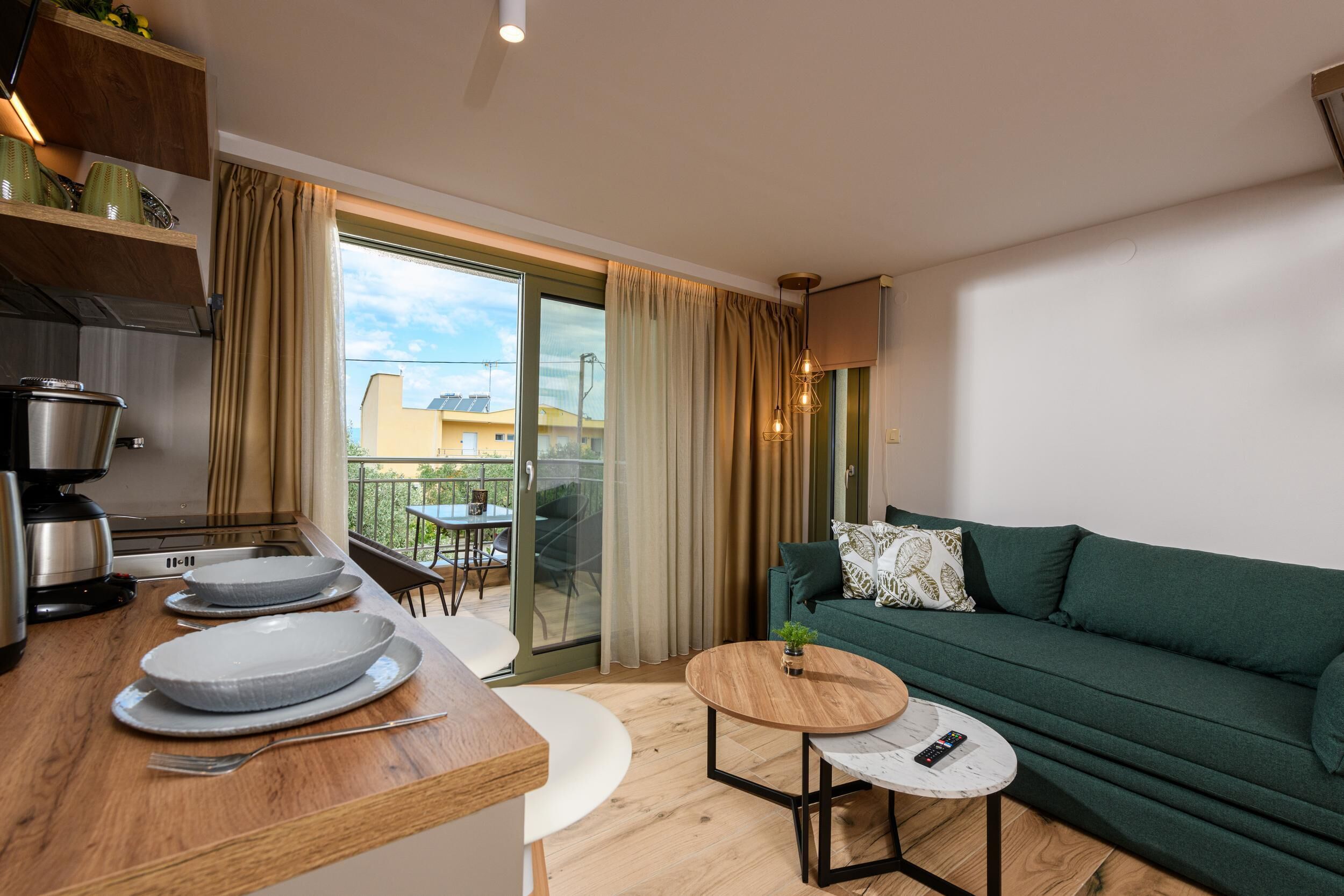 A modern living room with a green sofa, a wooden coffee table, and a kitchen area with a stove and plates.
