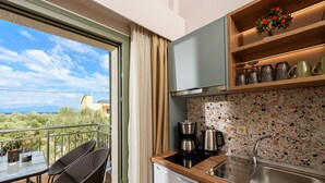 A compact kitchen with a built-in dishwasher, a coffee maker, and a sink. There's a balcony with a chair and a table, and a view of the outdoors. - The Olive Land (Thasos)