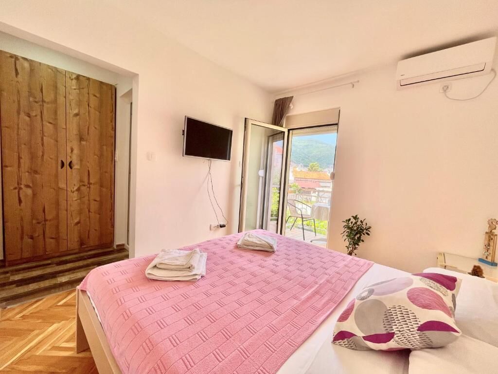 A bedroom with a bed, a TV, a sliding glass door, and a wooden wardrobe.