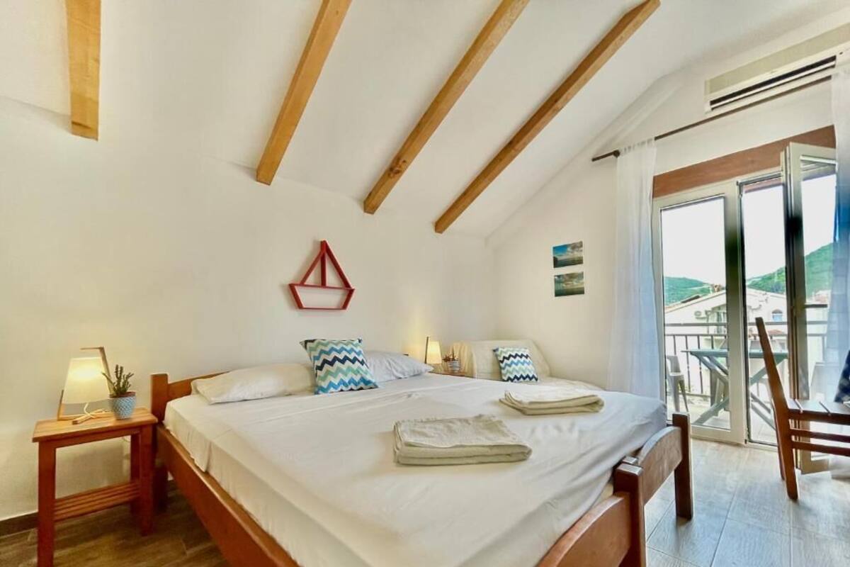 A bedroom with a wooden bed, a nightstand, a red geometric wall decoration, and a view of a balcony with outdoor furniture.