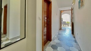 A hallway with a tiled floor, a wooden door, and a mirror on the wall. - Garden House Budva (Budva)