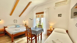 A room with two beds, a dining table, and a small table with a lamp. - Garden House Budva (Budva)