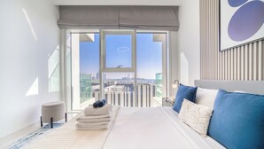 Habitación de hotel moderna con una cama grande, vistas de la ciudad y un balcón con barandilla.