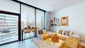 A modern living room with a large window, a sofa set, a dining table with chairs, and decorative items. - Modern Studio | Burj Khalifa View (Dubai)