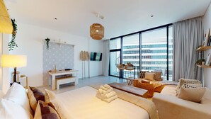 A modern hotel room with a large bed, a desk, a balcony with wicker furniture, and a city view. - Modern Studio | Burj Khalifa View (Dubai)