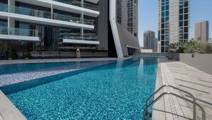 A modern building with a pool area, featuring a clear blue pool, a wooden deck, and a glass railing. - Modern Studio | Burj Khalifa View (Dubai)