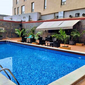 A swimming pool with lounge chairs and potted plants, surrounded by a building with a tiled exterior.