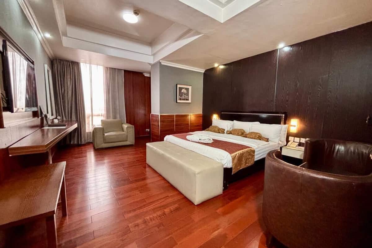 A hotel room with a large bed, a desk, a chair, and a sofa.