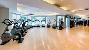 A gym with exercise equipment, large windows, and a wooden floor.