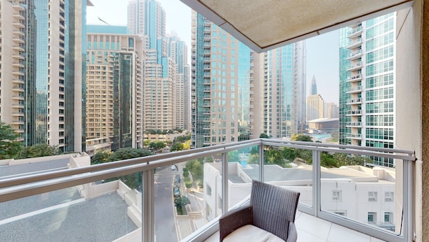 A balcony with a view of high-rise buildings, a chair, and a railing.