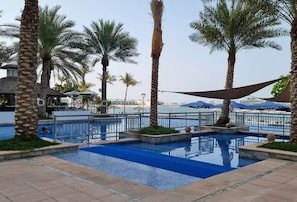 A pool area with palm trees, a clear sky, and a view of the sea. - Luxury 2BR | Palm Jumeirah | Pool Access (Dubai)
