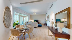 A modern living room with a dining area, large windows, a chandelier, and a large mirror. - Luxury 2BR | Palm Jumeirah | Pool Access (Dubai)