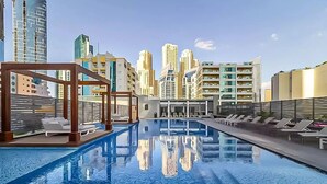 Ein Pool auf dem Dach mit Blick auf die Stadt, Liegestühle und eine Holz-Pergola.