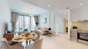 A modern apartment with a dining area, a living room with a sofa and a coffee table, a kitchen with a stove and cabinets, and large windows offering a city view. - Luxe 1BR w/ Stunning Sea Views and Infinity Pool (Dubai)