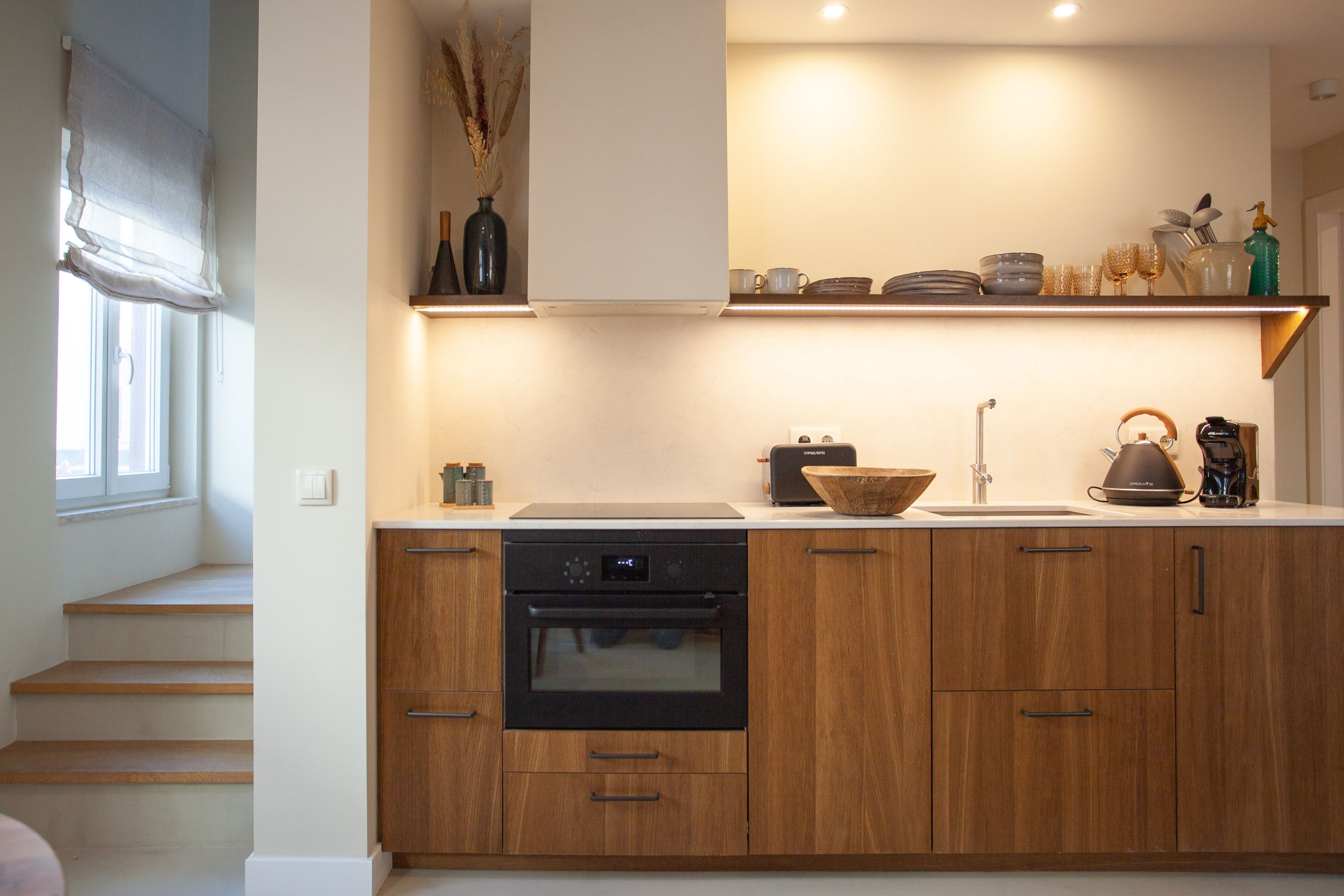 A modern kitchen with wooden cabinets, a built-in oven, and a countertop with various kitchen items.