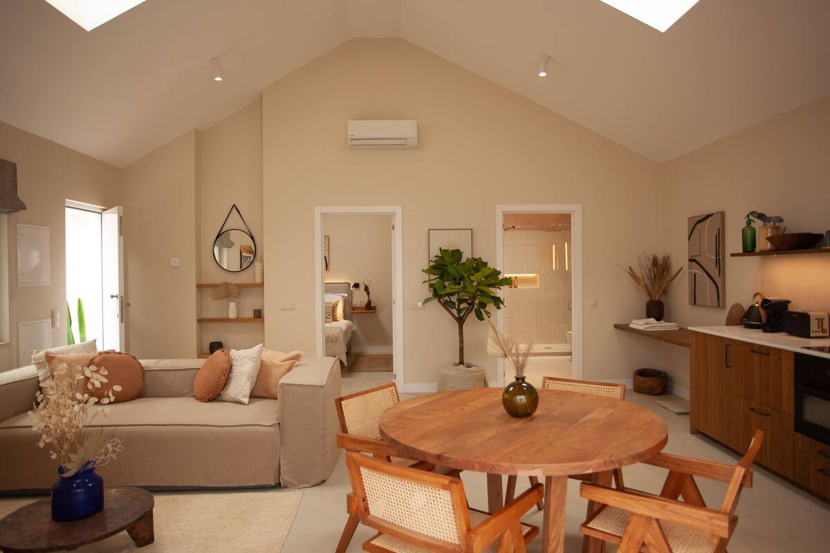 A spacious living area with a high ceiling, a wooden dining table, and a cozy sofa.