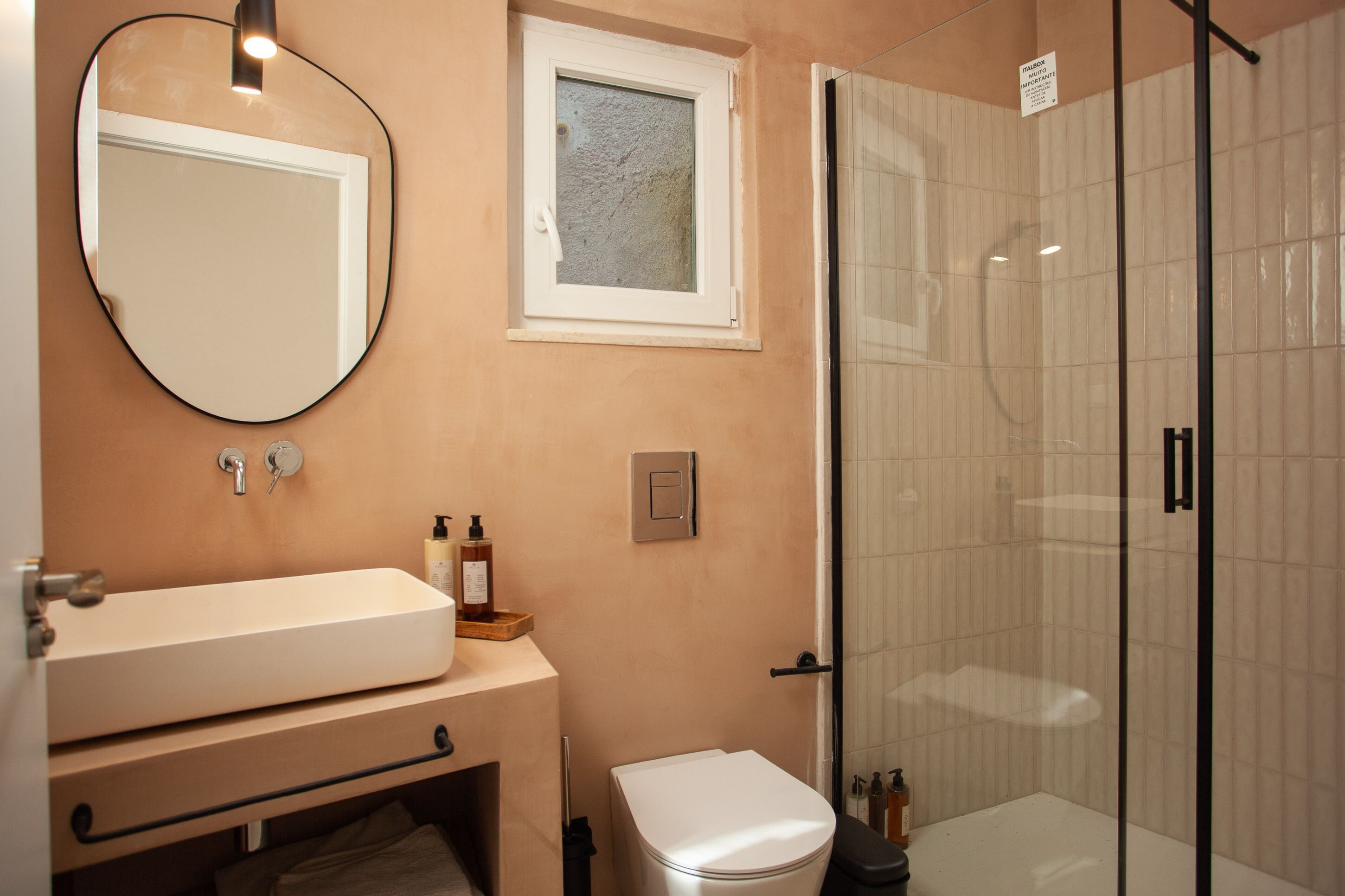 A bathroom with a sink, mirror, window, and shower.