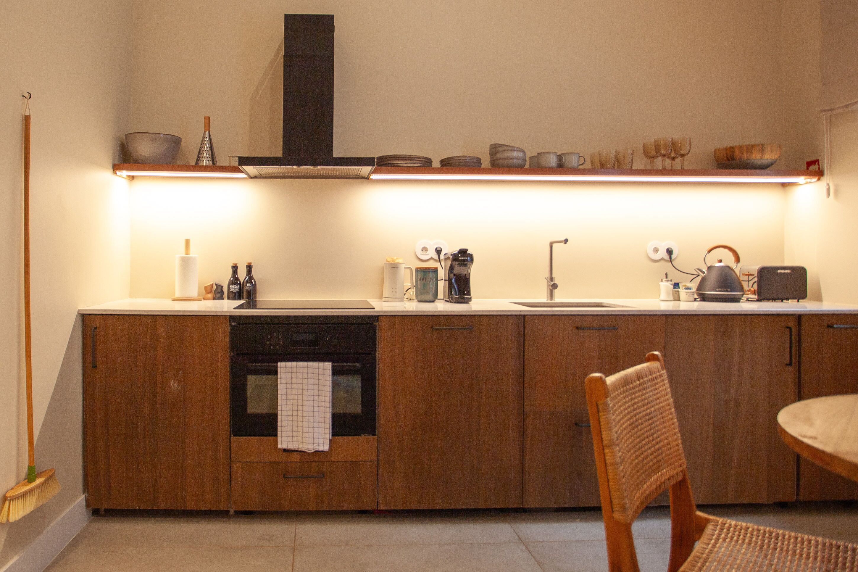 Una cocina moderna con armarios de madera, horno empotrado, cafetera y un comedor con una silla de mimbre.