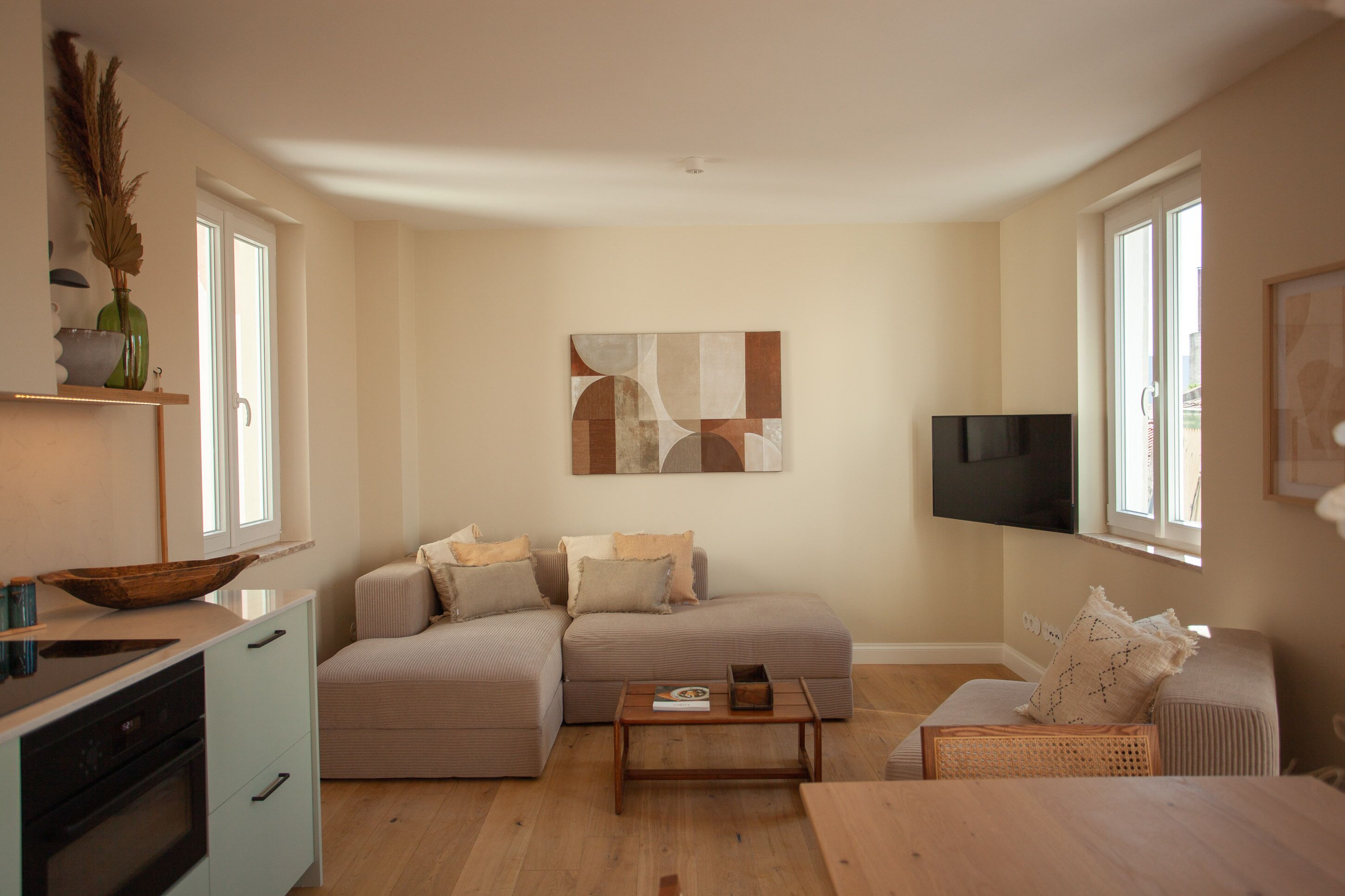 En moderne stue med sofa, sofabord og et fladskærms-tv på væggen.