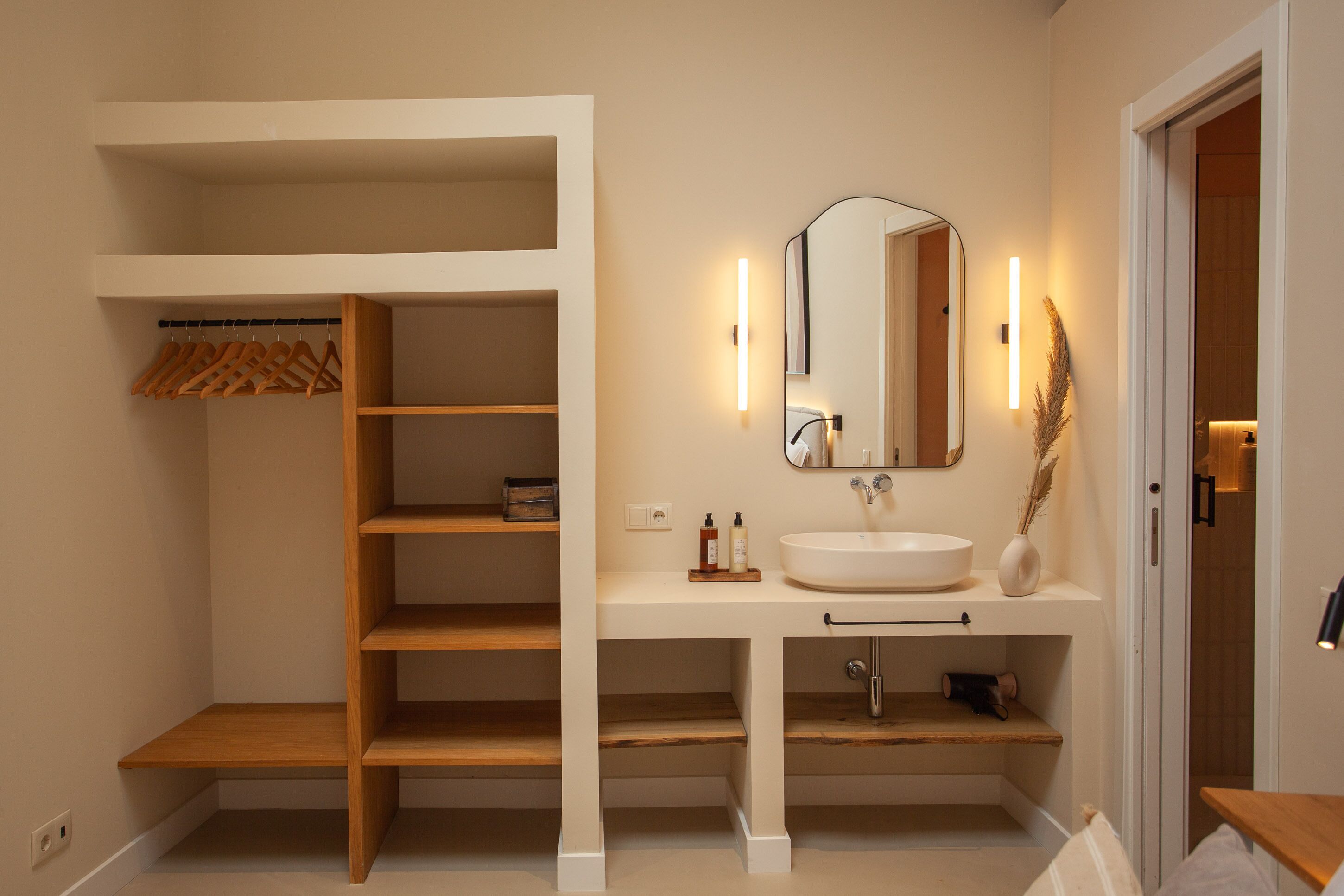 A modern bathroom with a white vanity, a large mirror, and a wooden shelving unit.