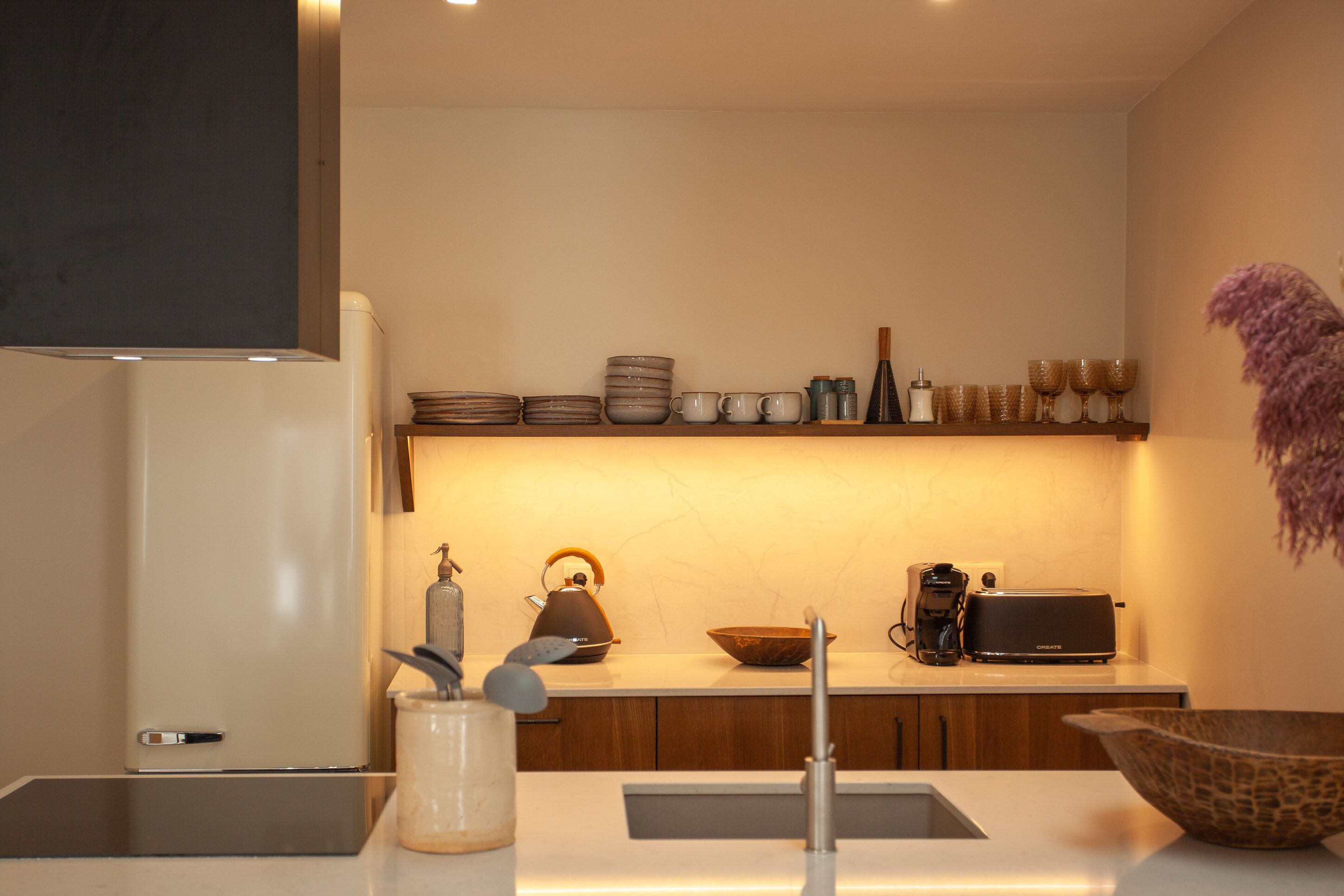 Une cuisine moderne équipée d’un four encastré, d’une machine à café, d’un grille-pain, ainsi que de différents bols et tasses disposés sur le plan de travail.