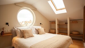 A bedroom with a large bed, a skylight, a round window, and built-in shelving. - Vila Rodrigues (Lisbon)