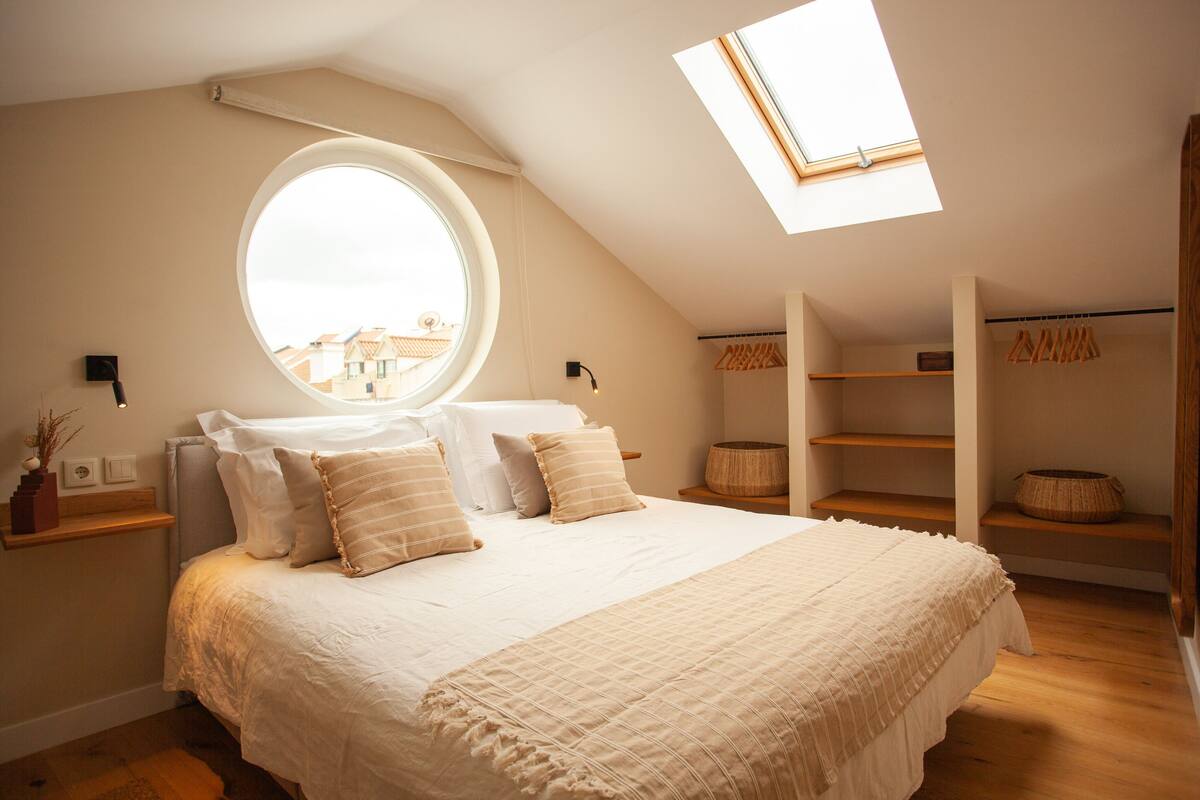 A bedroom with a large bed, a skylight, a round window, and built-in shelving.