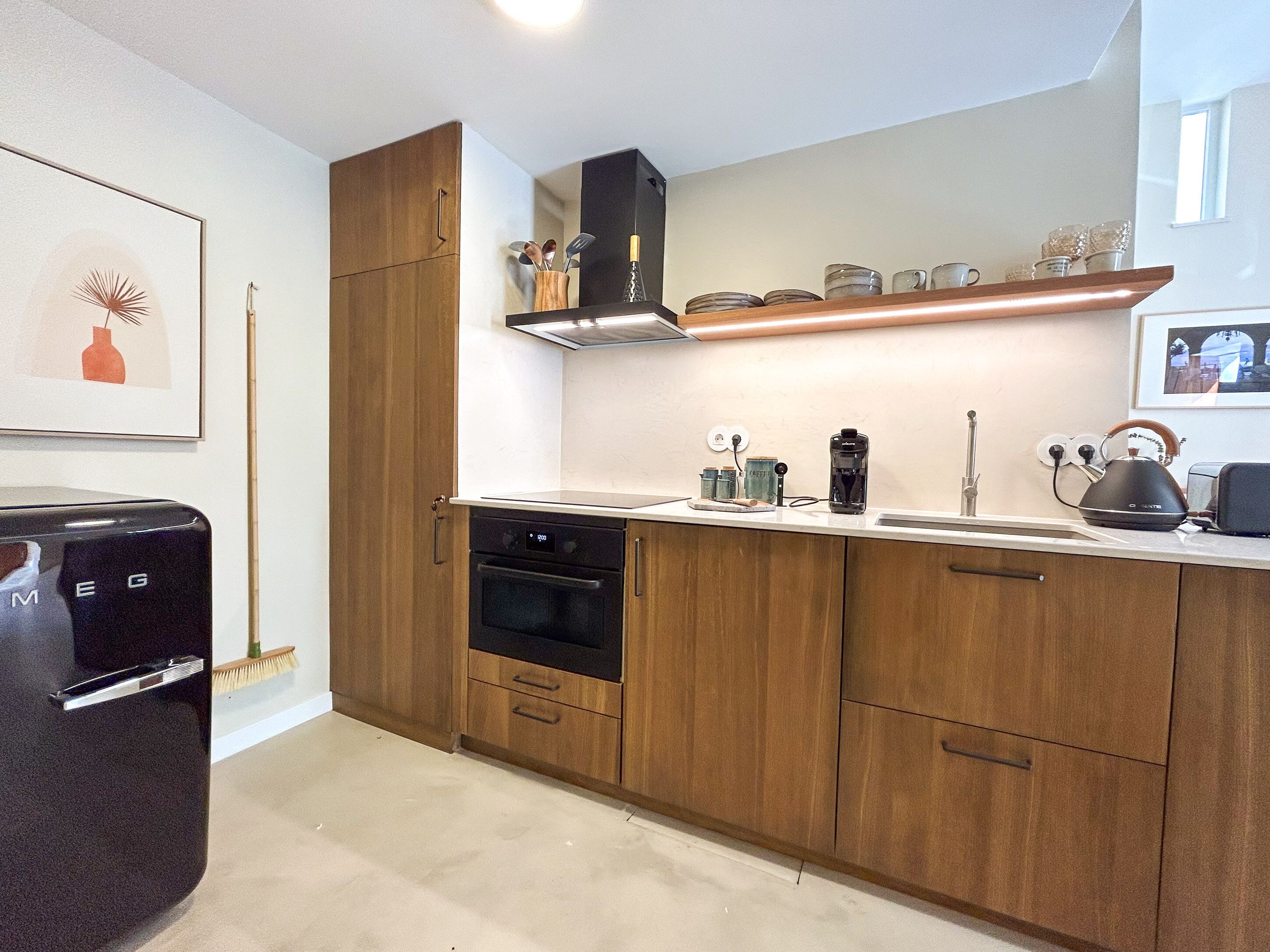 A modern kitchen with wooden cabinets, a built-in oven, a coffee machine, and a kettle on the countertop.