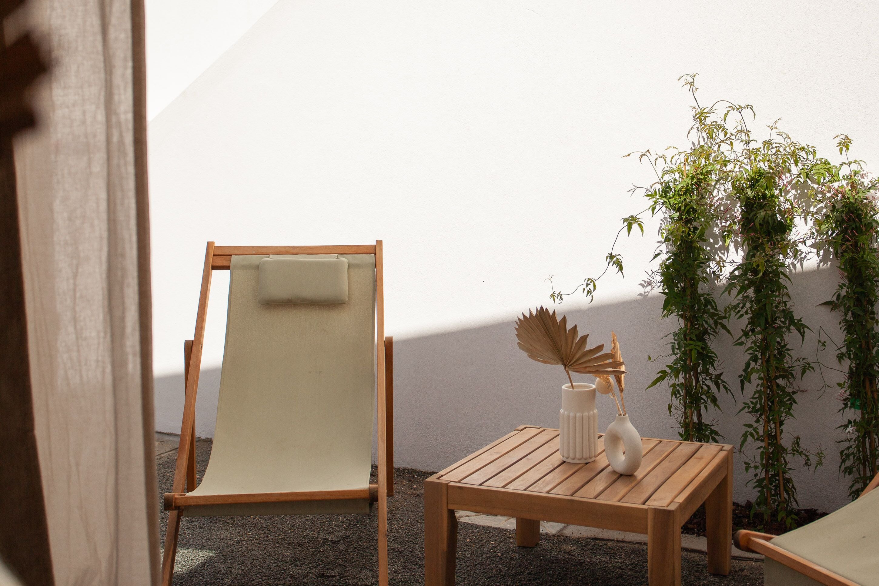 A wooden chair and table set against a white wall, with a potted plant beside the table.