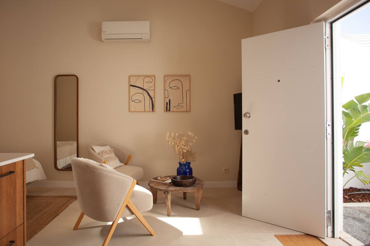 A modern bedroom with a bed, a chair, a small table with a vase, and artwork on the wall.