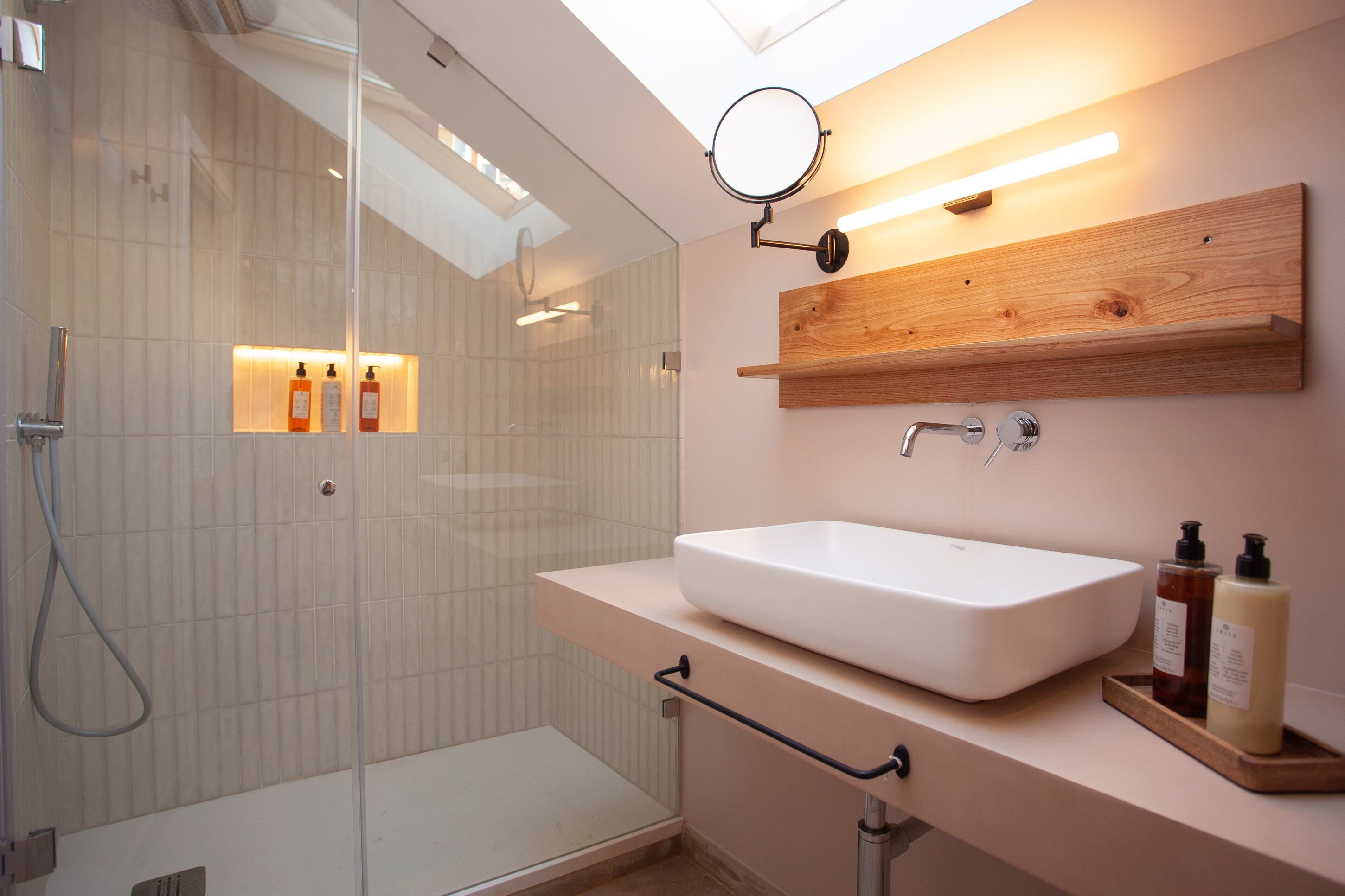 A modern bathroom with a glass shower enclosure, a white sink, and a wooden shelf above the sink.