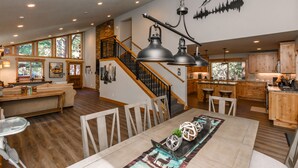 A spacious living area with a dining table, wooden flooring, and a staircase leading to a loft. - Clubhouse_On Hole 10, Hot Tub, Sauna, GameRoom, Pool Table, Arcades, Walk To Hole 1 & Driving Range (Truckee)