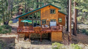A wooden cabin with a deck, large windows, and a stone foundation. - Clubhouse_On Hole 10, Hot Tub, Sauna, GameRoom, Pool Table, Arcades, Walk To Hole 1 & Driving Range (Truckee)