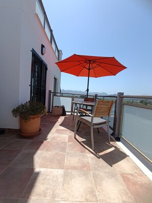 Een balkon met een tafel, stoelen, een bloempot en een parasol.