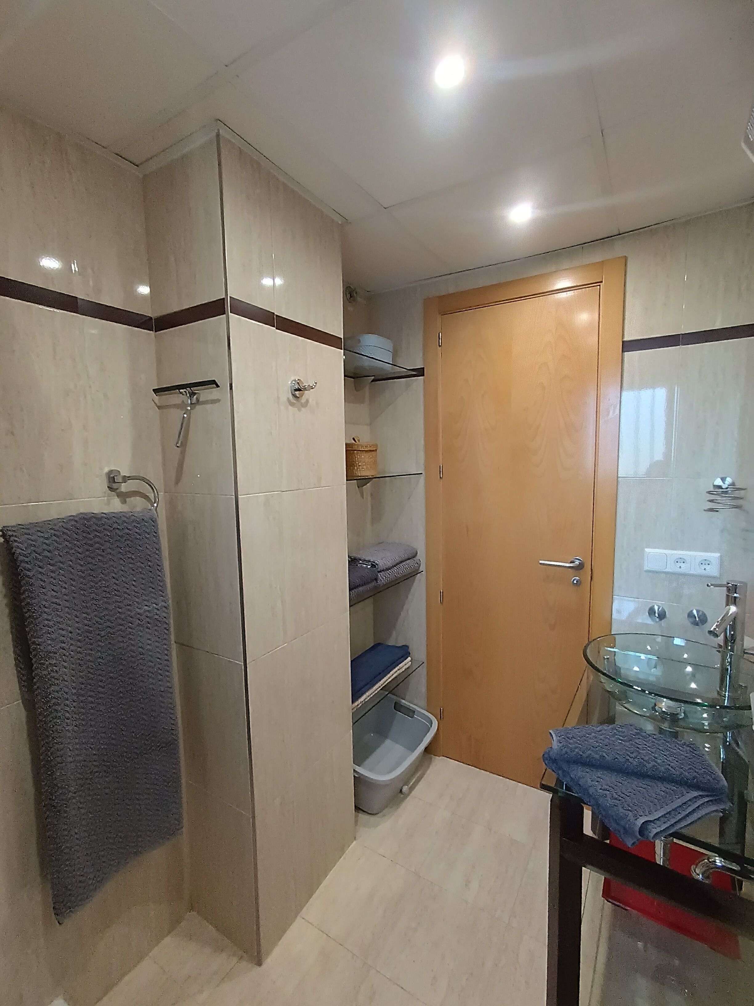 Ein Badezimmer mit einem Glaswaschbecken, einem Handtuchhalter, einer Dusche und einer Tür mit Griff.