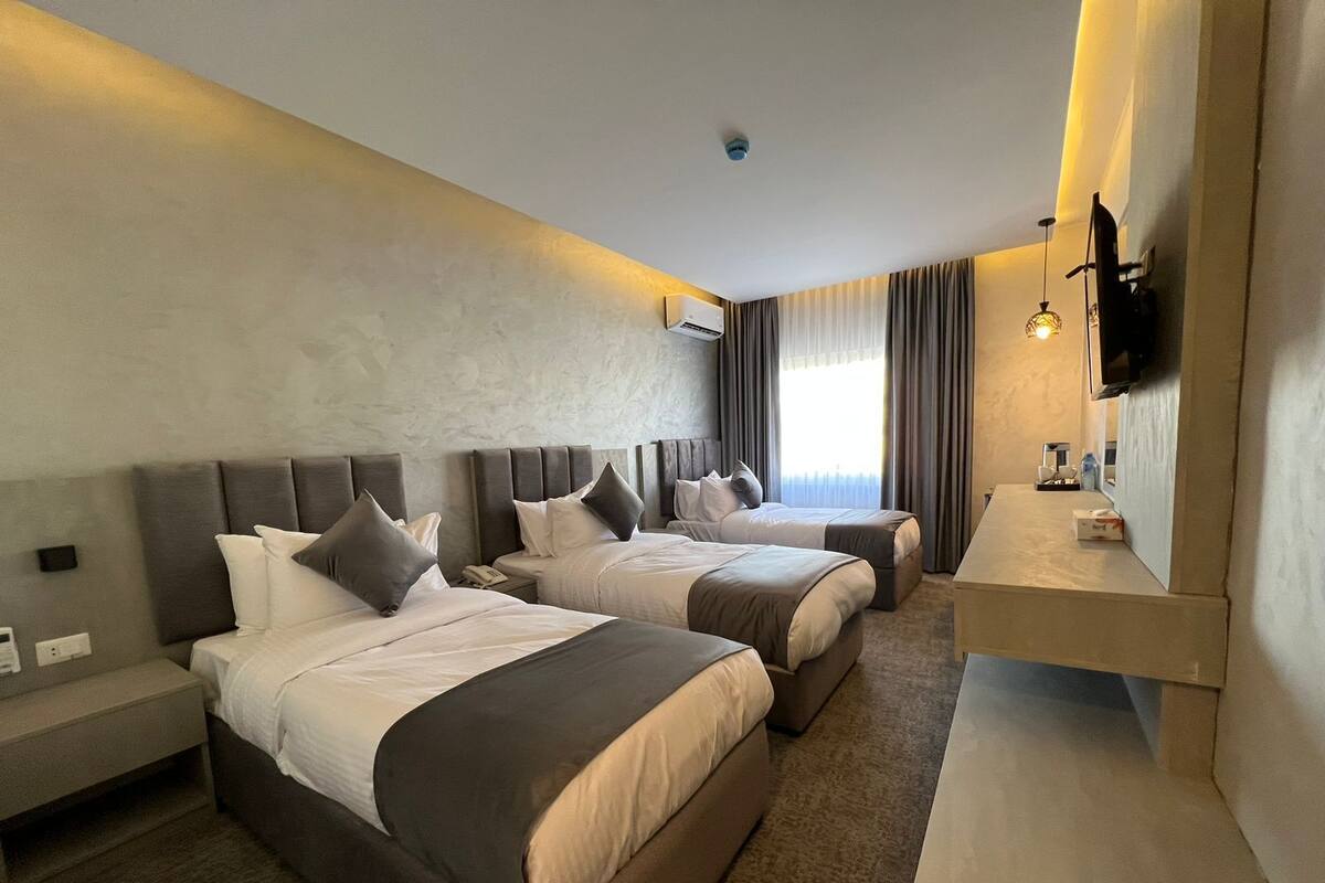 A hotel room with two beds, a desk, a TV, and a window with curtains.