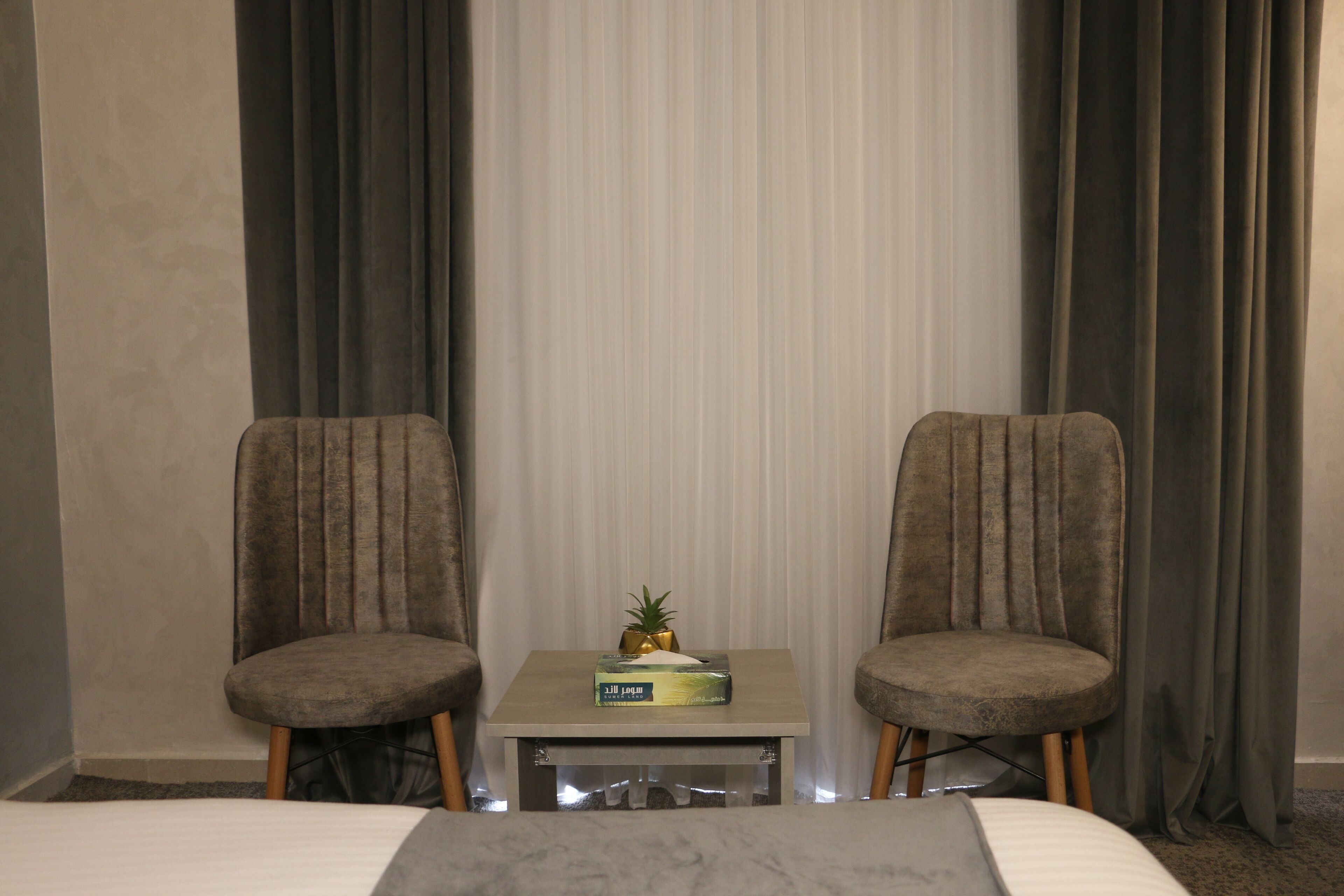 A hotel room with two armchairs, a small table with a pineapple and a box, and a bed with a marble headboard.