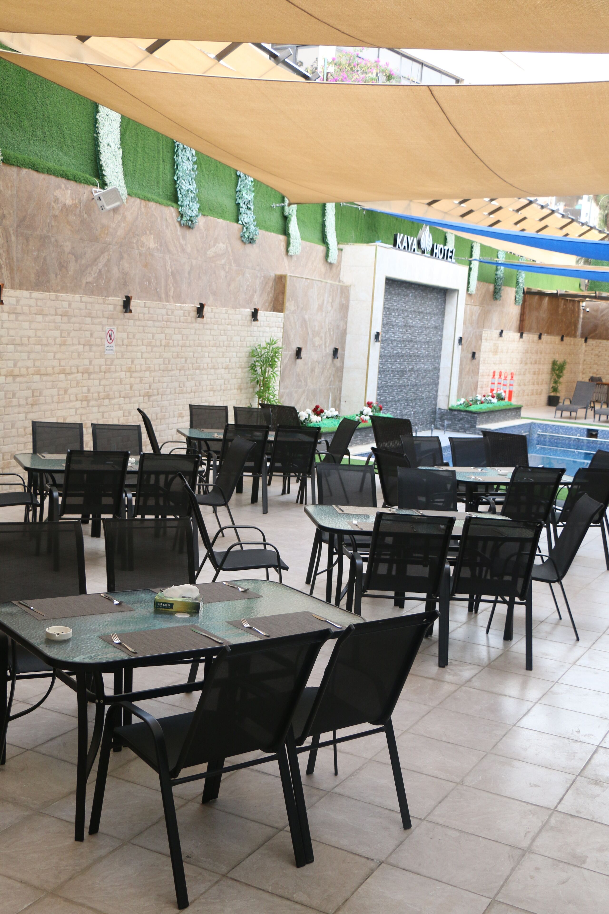 An outdoor seating area with tables and chairs, a pool, and a sign for KAYA HOTEL.