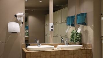 A bathroom with two sinks, a hair dryer, a mirror, and a potted plant.