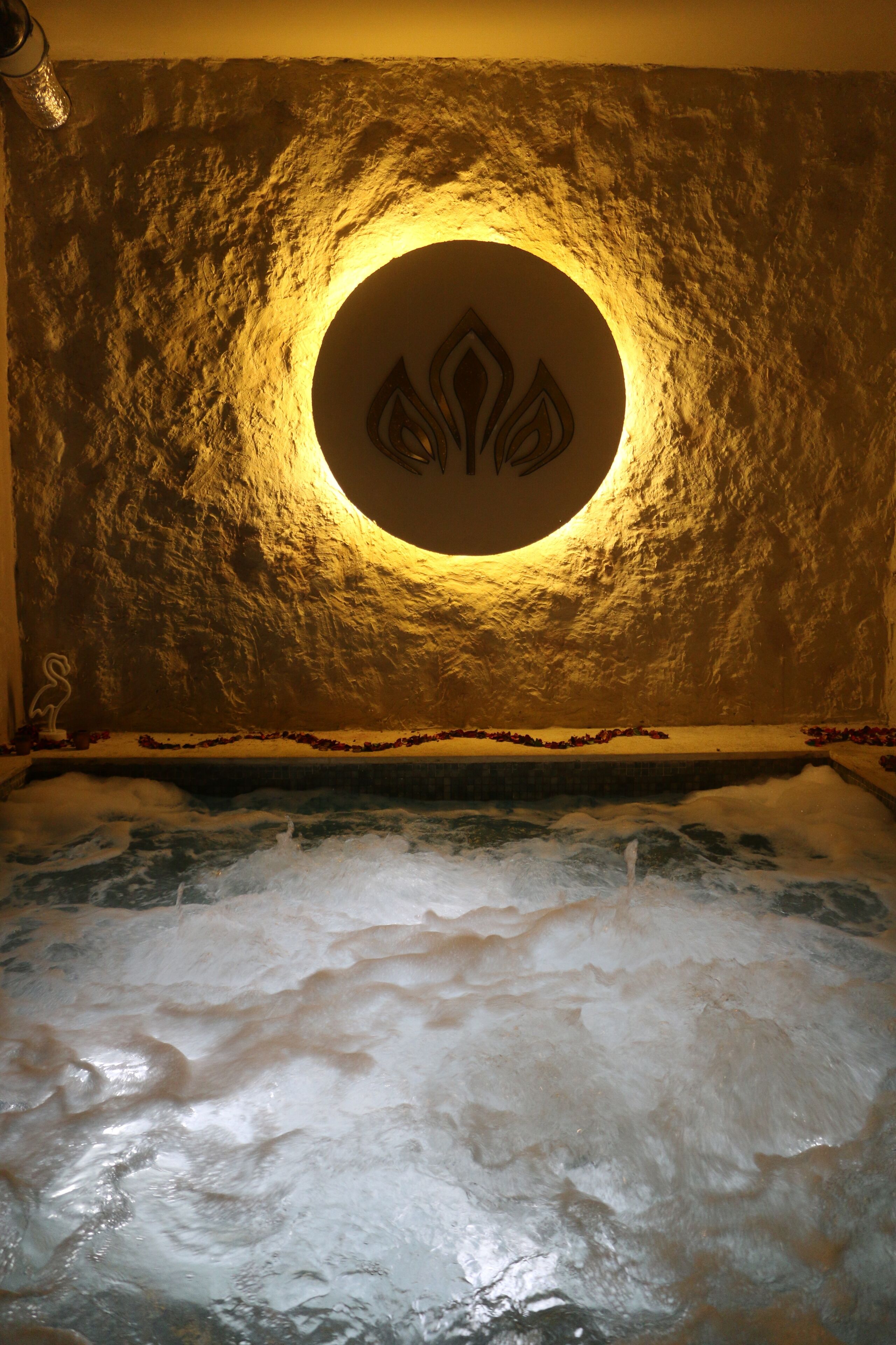 Ein Whirlpool mit kreisförmigem Design an der Wand, umgeben von einer strukturierten Wand und einem Pool.