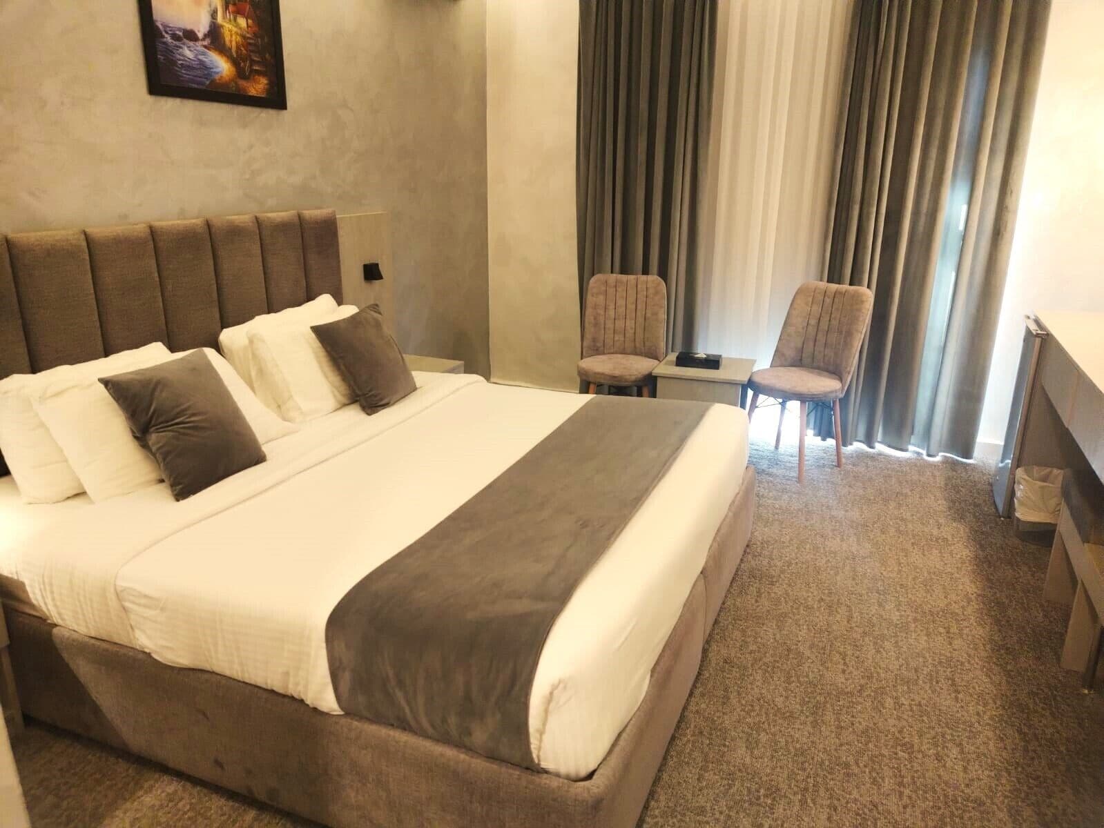 Habitació d'hotel amb un llit gran, dues cadires, una taula petita i un quadre al mur.