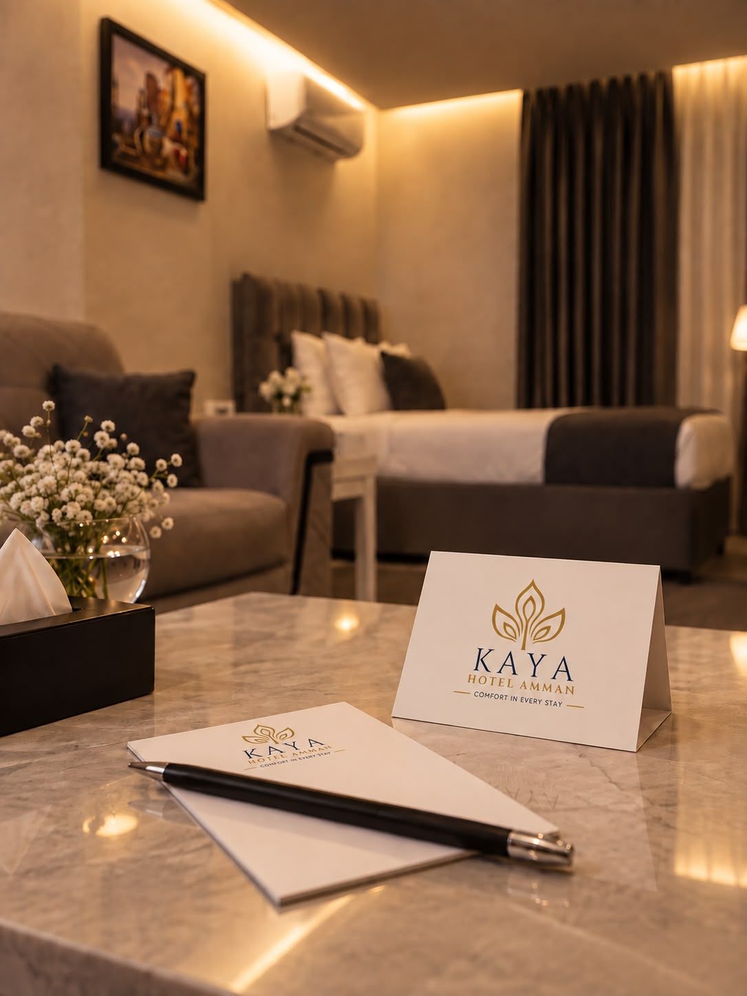 A hotel room with a bed, a sofa, a desk with a pen, a notepad, and a card on the desk.