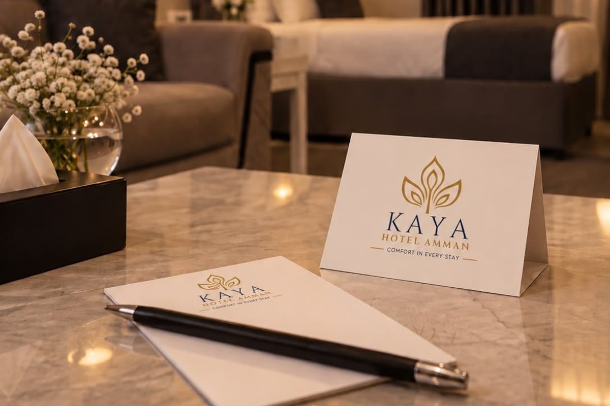 A hotel room with a bed, a sofa, a desk with a pen, a notepad, and a card on the desk.