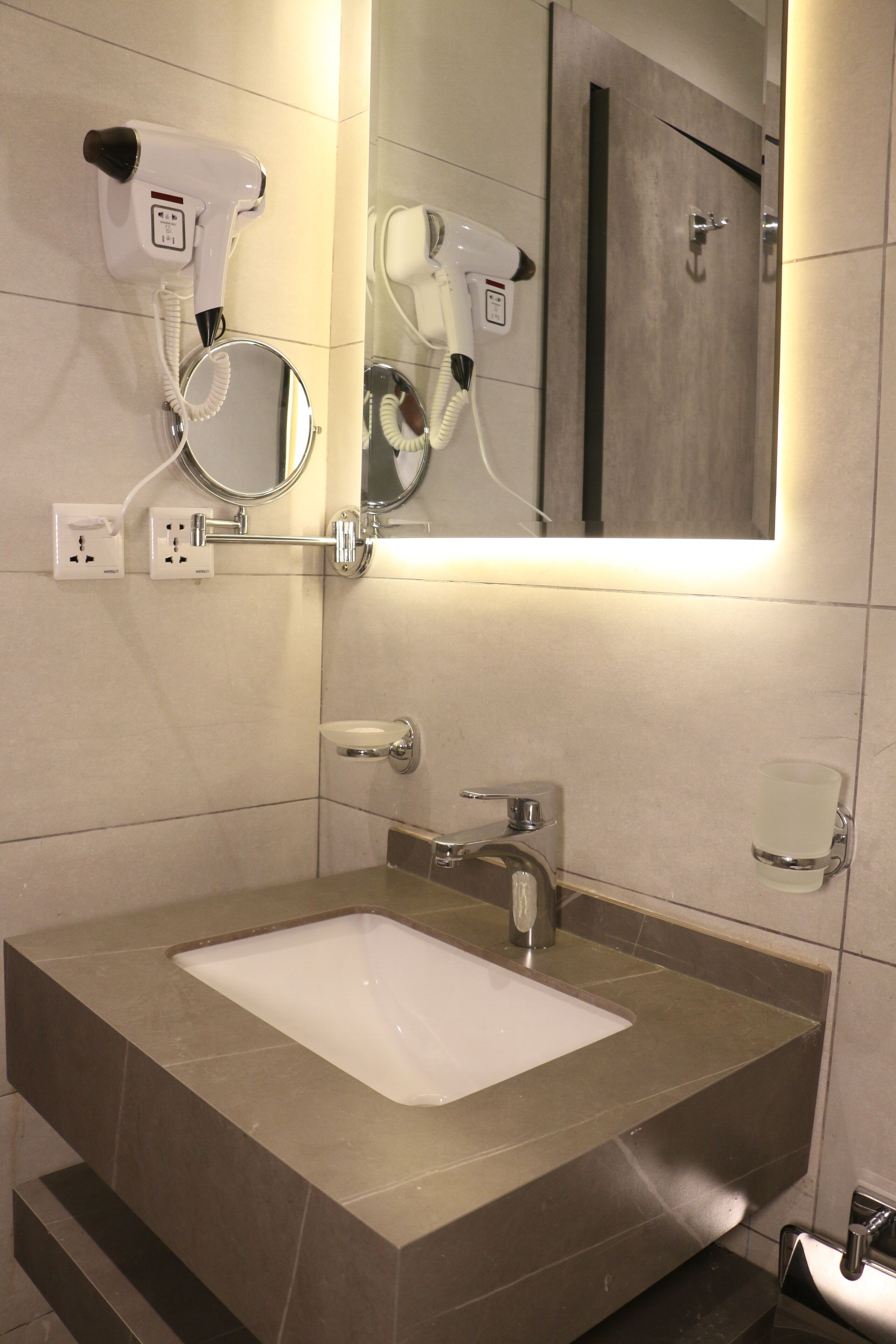 A modern bathroom with a large mirror, a hairdryer, and a sink.